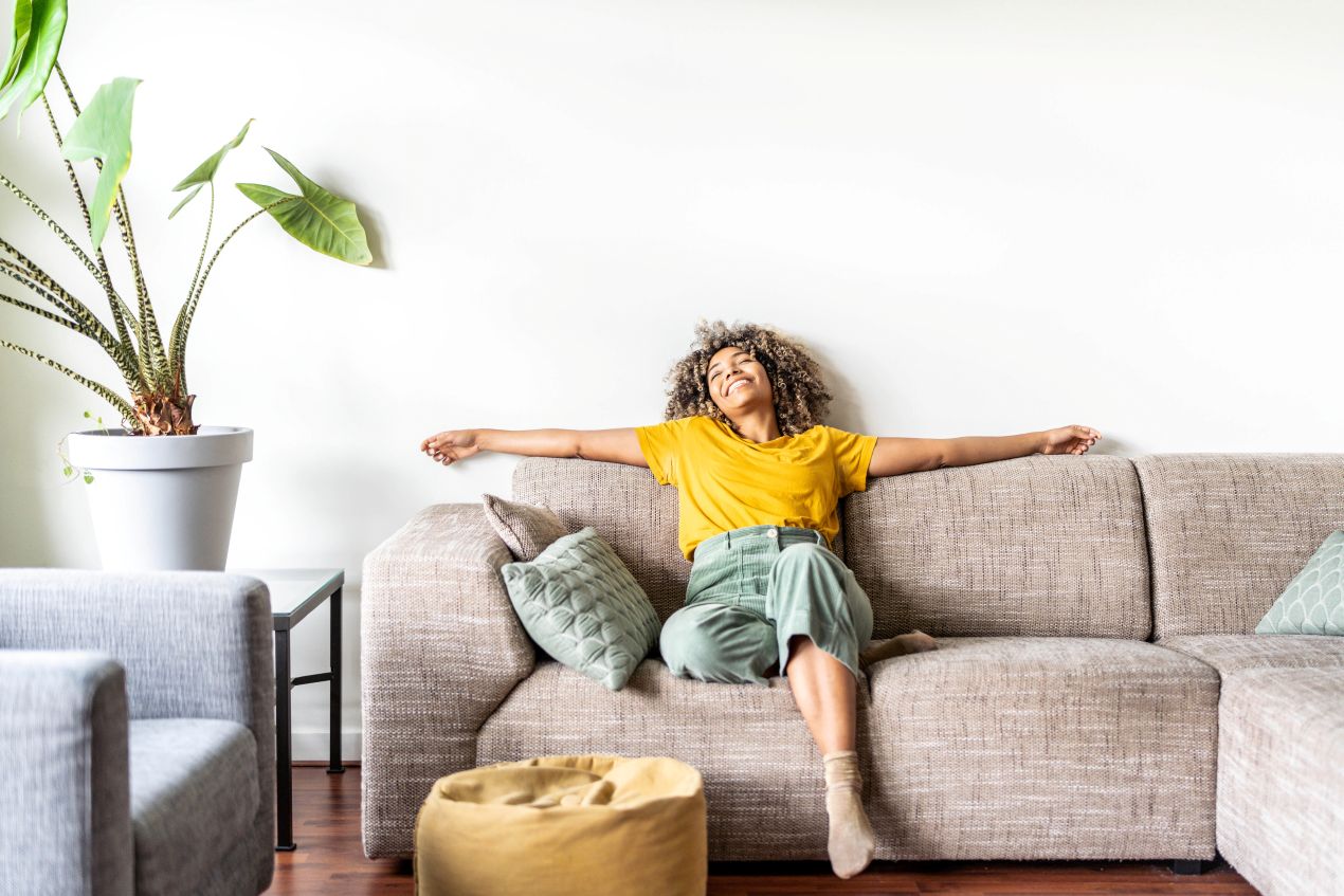 Eine glückliche Frau sitzt entspannt auf einem gemütlichen Sofa, umgeben von Pflanzen und Kissen – ein Symbol für ein neues, selbstbestimmtes Leben nach der Scheidung.