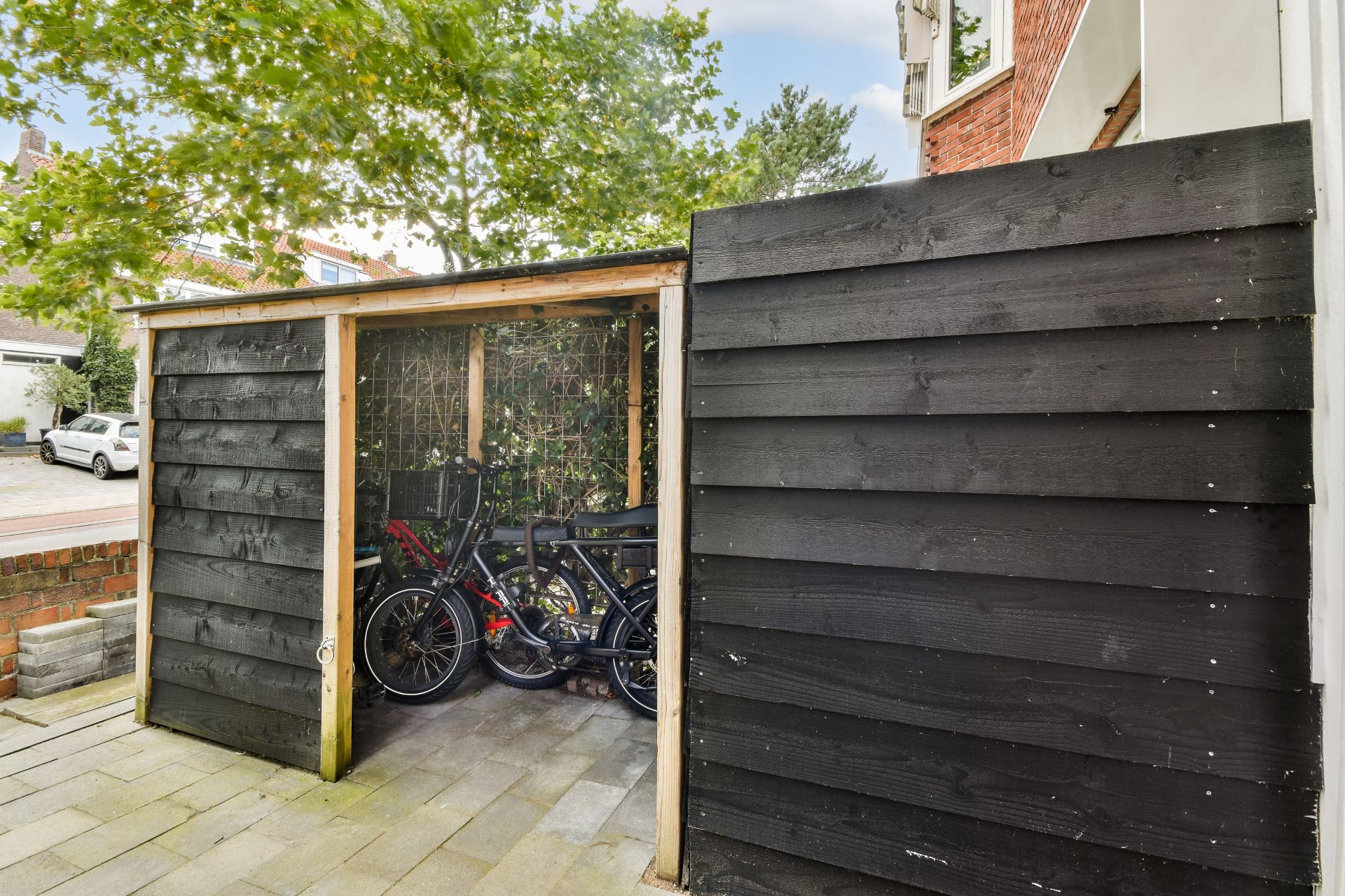 Schlichte Fahrradueberdachung aus schwarzem Holz mit E-Bikes im urbanen Vorgarten – funktionale Loesung mit natürlichem Sichtschutz.